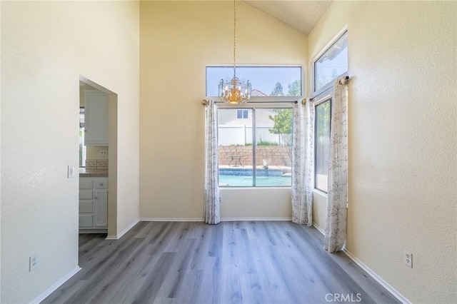 1573 E Brockton Ave, Redlands, CA 92374 - unfurnished dining area with a chandelier, wood finished floors, high vaulted ceiling, and baseboards