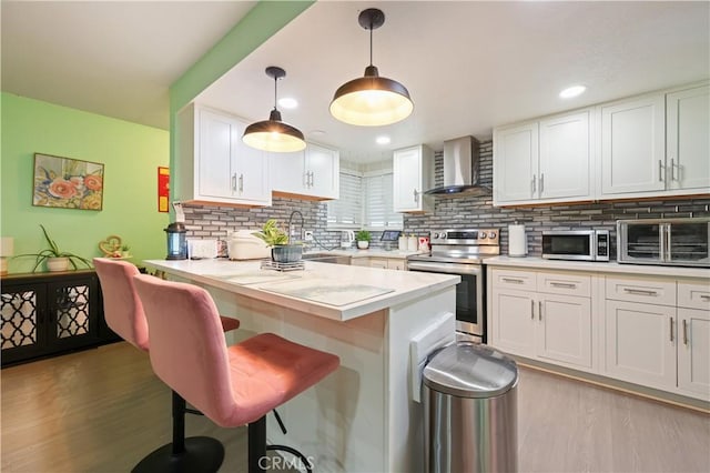 1257 E Grand Ave Unit A, Escondido, CA 92027 - kitchen featuring wall chimney range hood, appliances with stainless steel finishes, a sink, a breakfast bar area, and light wood-type flooring