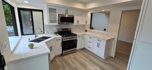 1364 Park Plaza Dr, Long Beach, CA 90804 - kitchen with appliances with stainless steel finishes, a sink, light wood-style floors, backsplash, and glass insert cabinets