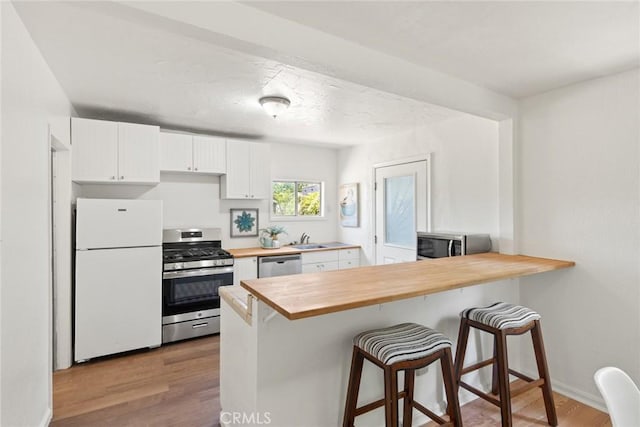1135 Oakdale St, Chico, CA 95928 - kitchen with appliances with stainless steel finishes, wooden counters, a sink, white cabinetry, and wood finished floors