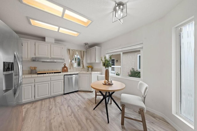 4938 Dulin Rd, Fallbrook, CA 92028 - kitchen with appliances with stainless steel finishes, under cabinet range hood, white cabinetry, light wood finished floors, and tile counters