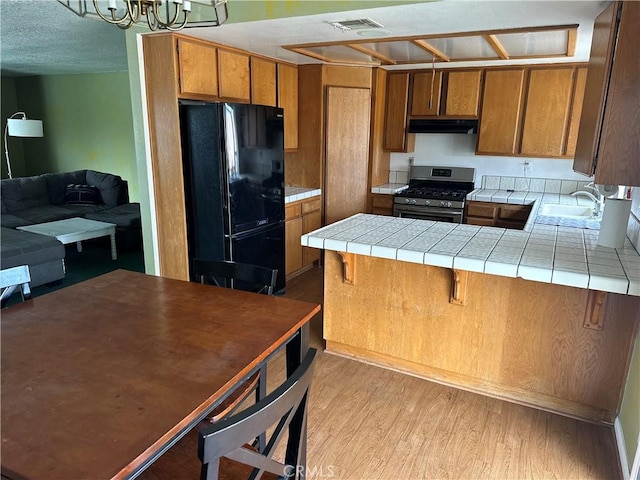 37824 Queensboro Ct, Palmdale, CA 93552 - kitchen with stainless steel range with gas stovetop, freestanding refrigerator, brown cabinetry, and light wood-style floors