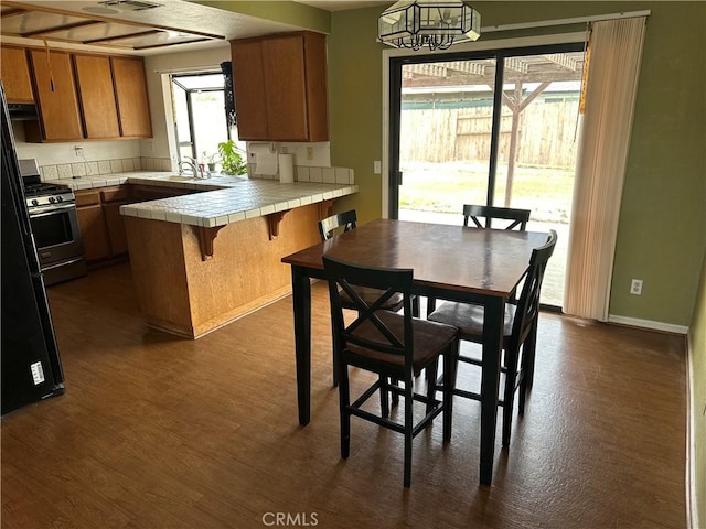 37824 Queensboro Ct, Palmdale, CA 93552 - kitchen with tile counters, brown cabinets, a peninsula, stainless steel gas range, and dark wood-style floors