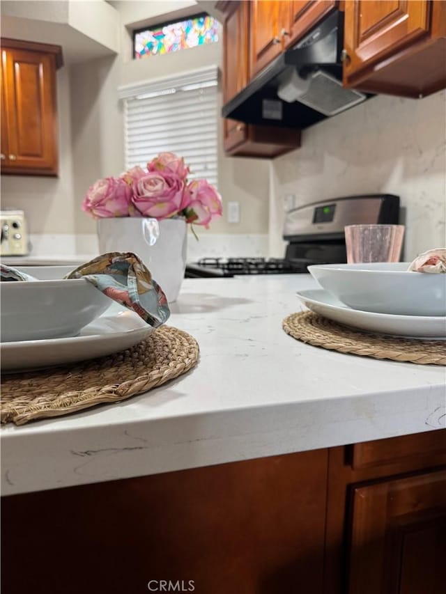 17191 Corbina Ln Unit 109, Huntington Beach, CA 92649 - kitchen featuring under cabinet range hood, stove, light countertops, and brown cabinetry