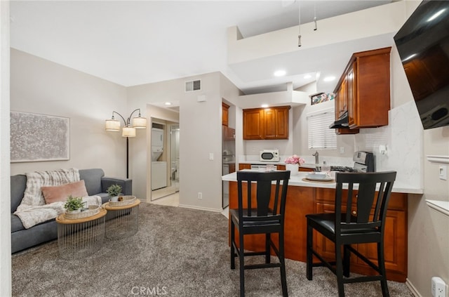 17191 Corbina Ln Unit 109, Huntington Beach, CA 92649 - kitchen featuring under cabinet range hood, brown cabinets, a peninsula, light countertops, and light colored carpet