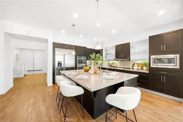 103 Sparrow, Irvine, CA 92618 - kitchen featuring built in appliances, a kitchen bar, a kitchen island with sink, light stone counters, and dark brown cabinets