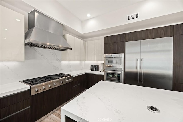 1279 Waterbrook Cir, Walnut, CA 91789 - kitchen with appliances with stainless steel finishes, wall chimney exhaust hood, dark brown cabinetry, tasteful backsplash, and modern cabinets