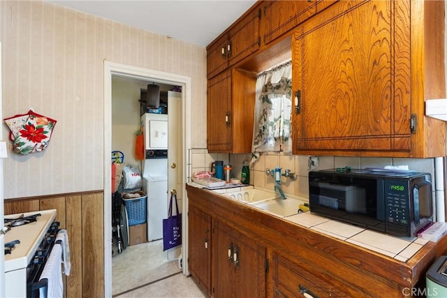602 Stanley Ave, Long Beach, CA 90814 - kitchen featuring stacked washer / dryer, black microwave, wallpapered walls, brown cabinetry, and gas range gas stove