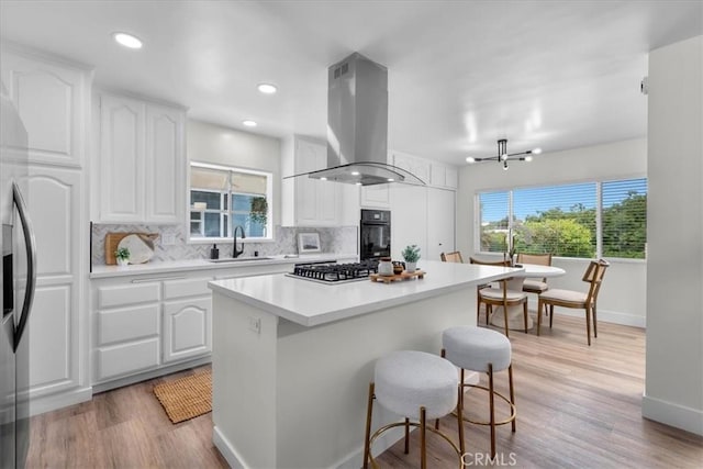 20512 Wayne Ave, Torrance, CA 90503 - kitchen featuring island exhaust hood, stainless steel appliances, decorative backsplash, white cabinetry, and a kitchen island