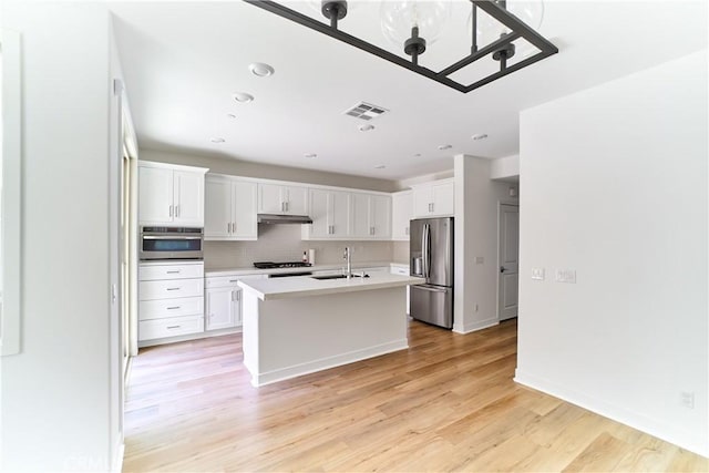 12392 Sandy Ct, Whittier, CA 90602 - kitchen with stainless steel appliances, light countertops, under cabinet range hood, tasteful backsplash, and light wood finished floors
