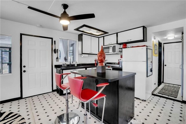 49490 Big Morongo Canyon Rd, Morongo Valley, CA 92256 - kitchen featuring white appliances, a sink, dark countertops, a center island, and white cabinetry