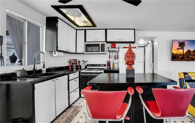 49490 Big Morongo Canyon Rd, Morongo Valley, CA 92256 - kitchen with stainless steel microwave, gas stove, dark countertops, a sink, and white cabinets