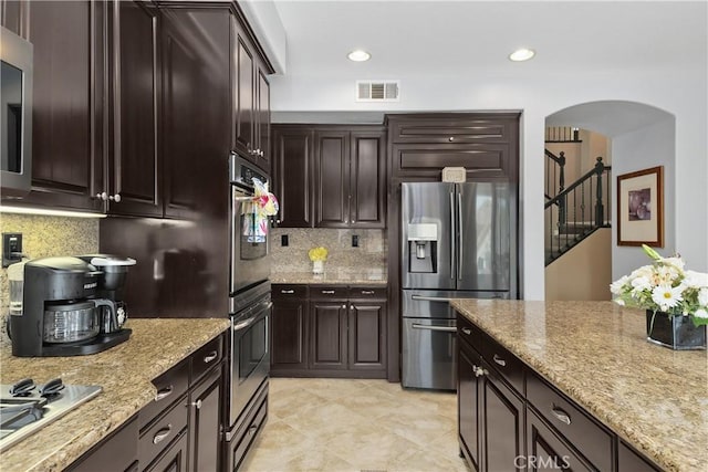 25079 Loring Rd, Wildomar, CA 92595 - kitchen featuring appliances with stainless steel finishes, backsplash, arched walkways, light stone countertops, and dark brown cabinetry
