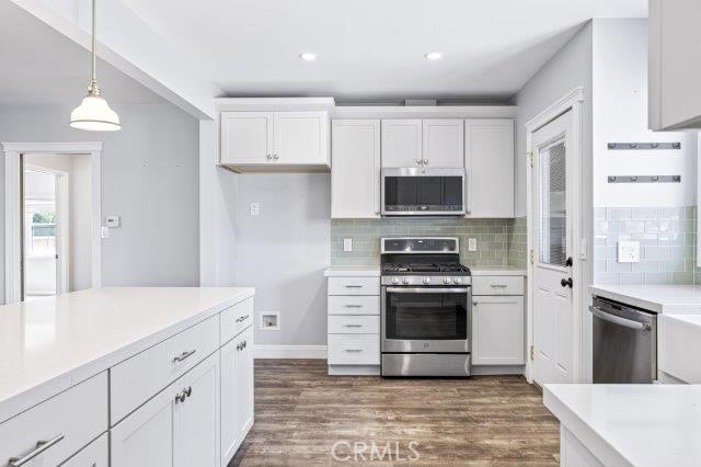 1501 W Baker Ave, Fullerton, CA 92833 - kitchen with appliances with stainless steel finishes, white cabinets, dark wood-type flooring, decorative light fixtures, and tasteful backsplash