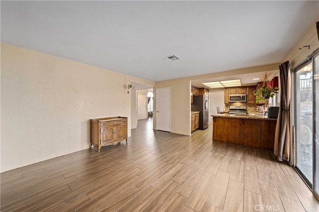 43816 Fallon Dr, Lancaster, CA 93535 - kitchen featuring appliances with stainless steel finishes, open floor plan, light wood-style flooring, brown cabinetry, and a peninsula