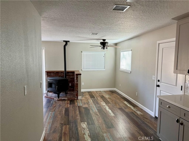 18083 Deodar St, Hesperia, CA 92345 - unfurnished living room featuring dark wood-style flooring, a ceiling fan, a wood stove, and a textured ceiling
