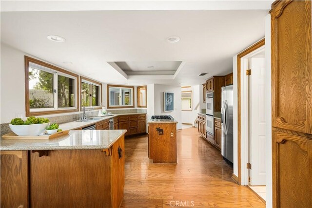 32022 Via Pavo Real, Coto De Caza, CA 92679 - kitchen featuring stainless steel appliances, brown cabinets, light wood finished floors, a raised ceiling, and a peninsula