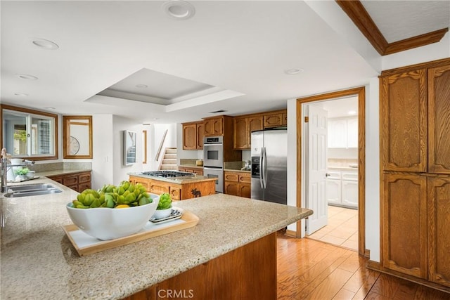 32022 Via Pavo Real, Coto De Caza, CA 92679 - kitchen with appliances with stainless steel finishes, a tray ceiling, a sink, light wood-type flooring, and brown cabinetry