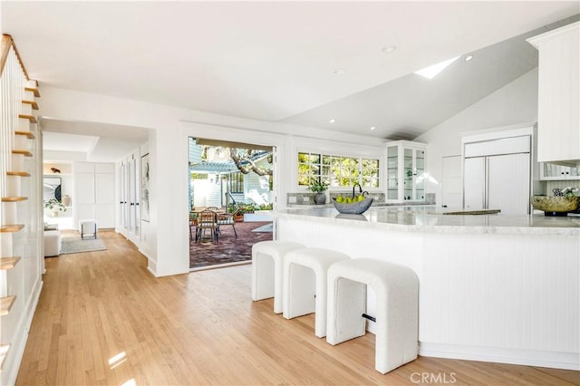 432 Holly St, Laguna Beach, CA 92651 - kitchen featuring light wood-style flooring, white cabinets, light stone countertops, a kitchen breakfast bar, and vaulted ceiling