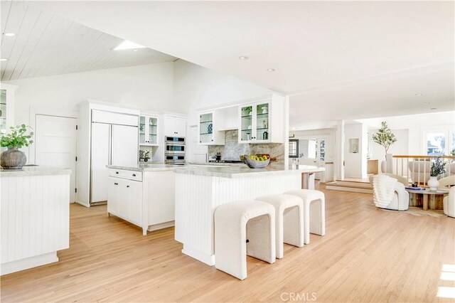 432 Holly St, Laguna Beach, CA 92651 - kitchen with light wood finished floors, a kitchen island, backsplash, white cabinets, and double oven