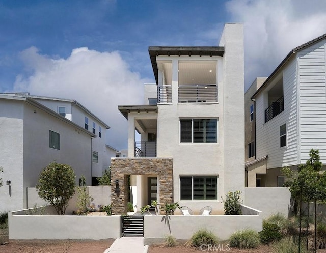 109 Pitch, Irvine, CA 92618 - modern home featuring a fenced front yard, a balcony, stucco siding, and stone siding