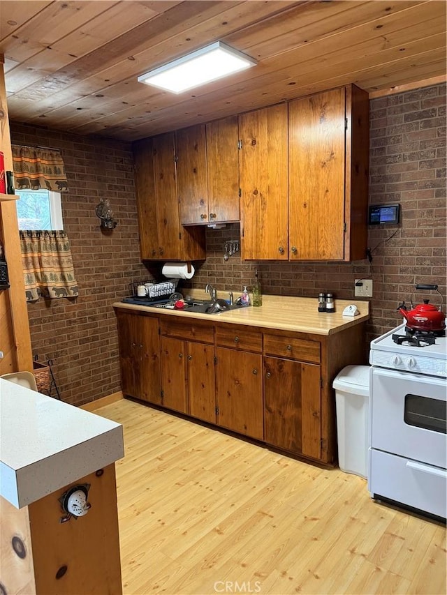 98011 Maine Rd, Kennedy Meadows, CA 93527 - kitchen with white range with gas cooktop, brick wall, light wood finished floors, brown cabinets, and wood ceiling