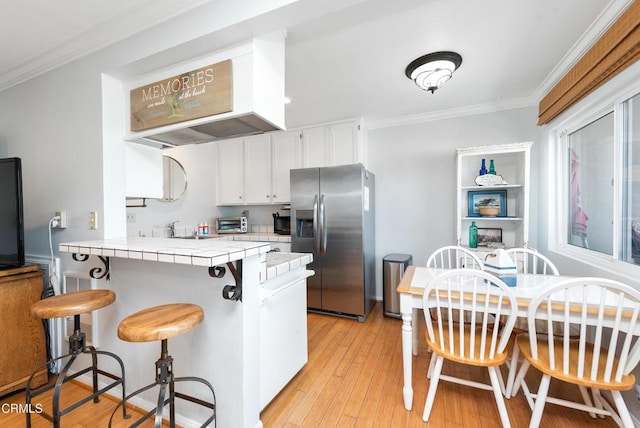 4975 Sandyland Rd Unit 302, Carpinteria, CA 93013 - kitchen with stainless steel fridge, tile countertops, white cabinetry, a peninsula, and crown molding