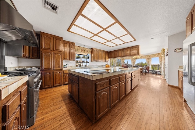 2360 Oakleaf Canyon Rd, Walnut, CA 91789 - kitchen with stainless steel appliances, exhaust hood, tile countertops, a center island, and light wood-style floors