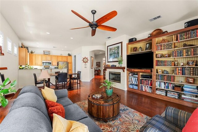 1574 Litchfield Ct, Banning, CA 92220 - living area with ceiling fan, arched walkways, dark wood finished floors, a glass covered fireplace, and baseboards