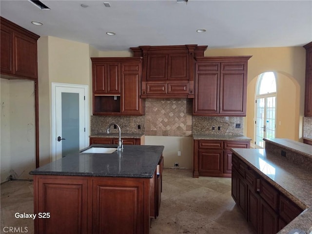 10040 Mattock Ave, Downey, CA 90240 - kitchen with a sink, decorative backsplash, dark stone countertops, an island with sink, and arched walkways