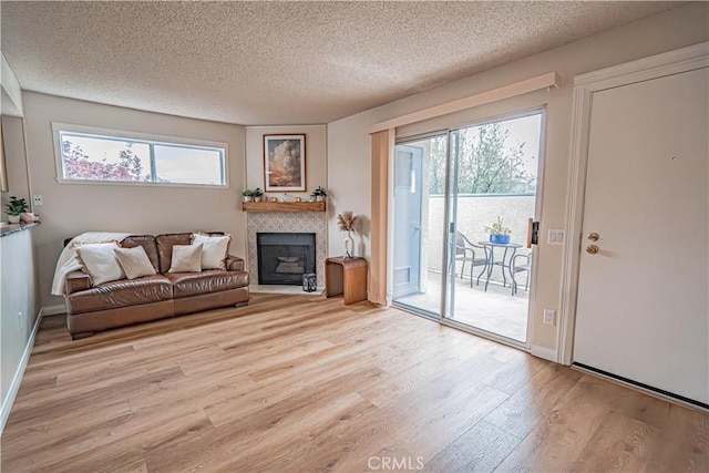 18209 Sierra Unit 45, Canyon Country, CA 91351 - living room with light wood-style flooring, a textured ceiling, healthy amount of natural light, a tile fireplace, and baseboards