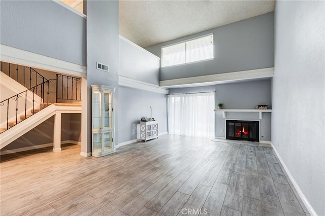 1320 Shadow Cir, Upland, CA 91784 - unfurnished living room featuring wood finished floors, a towering ceiling, stairway, a glass covered fireplace, and baseboards