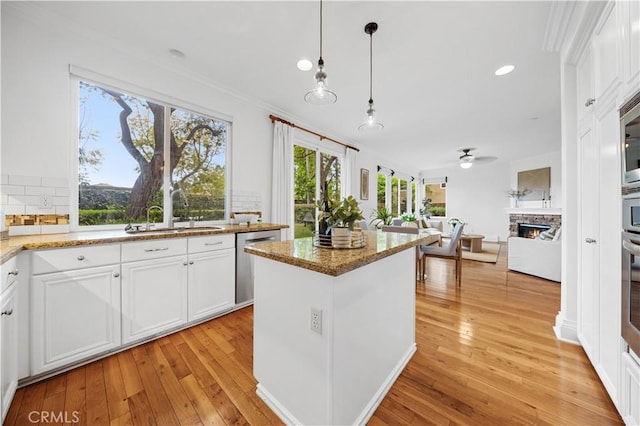 26 Middleton, Irvine, CA 92620 - kitchen with stainless steel dishwasher, a sink, a fireplace, light wood-style floors, and crown molding