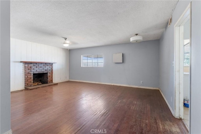 35921 80th St E, Littlerock, CA 93543 - unfurnished living room featuring wood finished floors, a textured ceiling, baseboards, and a brick fireplace