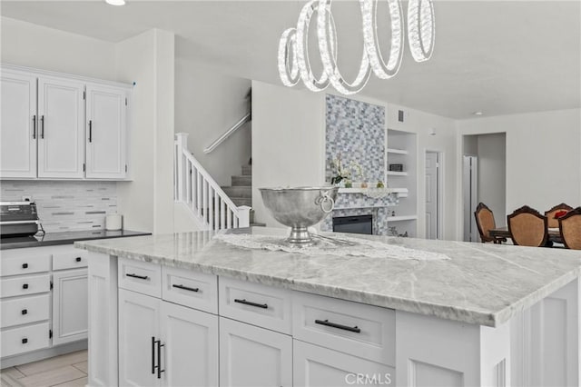 27051 Featherhill Dr, Corona, CA 92883 - kitchen featuring white cabinetry, backsplash, light stone countertops, decorative light fixtures, and a glass covered fireplace