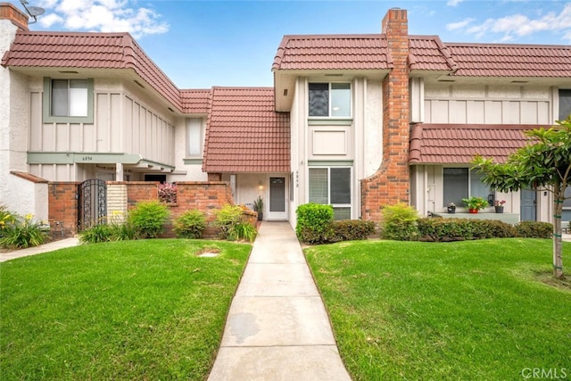 6898 Breton Way, Cypress, CA 90630 - townhome / multi-family property featuring a tile roof, board and batten siding, a chimney, a front lawn, and stucco siding