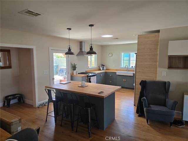 18334 Glenburn Ave, Torrance, CA 90504 - kitchen featuring butcher block countertops, stainless steel range with gas cooktop, wall chimney range hood, a breakfast bar, and wood finished floors