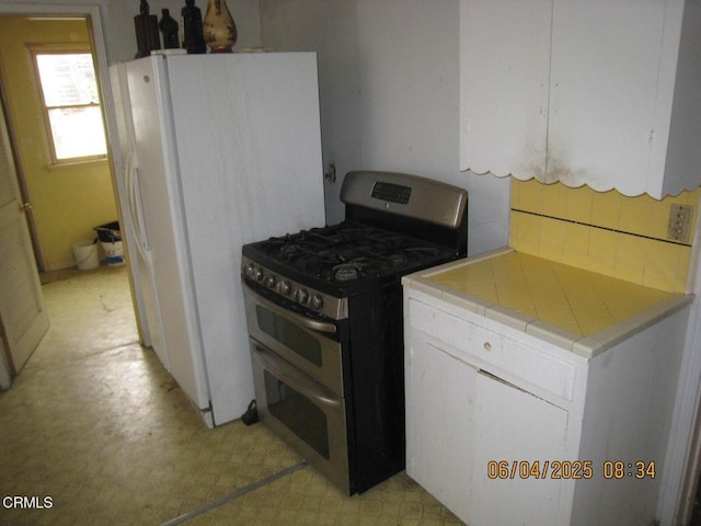 542 1st St, Fillmore, CA 93015 - kitchen with stainless steel range with gas cooktop, tile countertops, light floors, white cabinetry, and tasteful backsplash