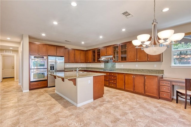 14939 Franklin Ln, Eastvale, CA 92880 - kitchen with stainless steel appliances, brown cabinetry, a chandelier, under cabinet range hood, and recessed lighting