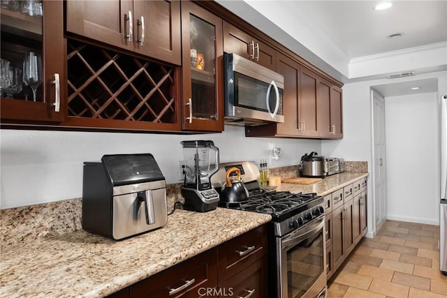 1675 W Lambert Rd Unit G, La Habra, CA 90631 - kitchen featuring appliances with stainless steel finishes, glass insert cabinets, light stone counters, dark brown cabinetry, and ornamental molding