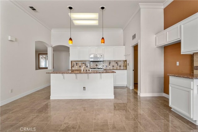 960 Hemingway Dr, Corona, CA 92878 - kitchen featuring white microwave, arched walkways, dark stone countertops, white cabinets, and ornamental molding