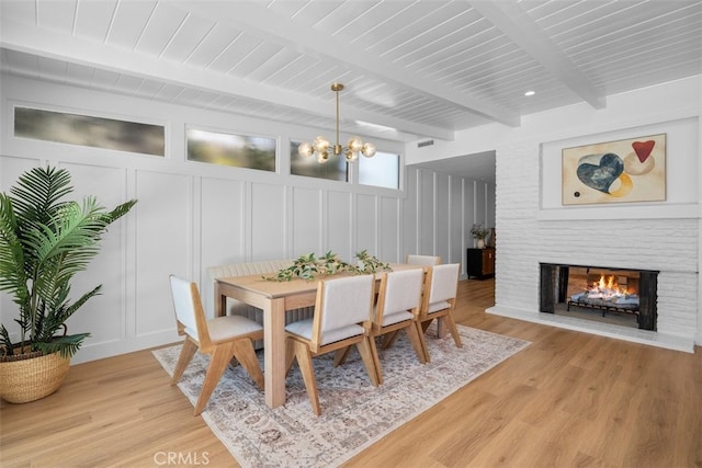 3830 Cedar Ave, Long Beach, CA 90807 - dining space featuring a chandelier, a decorative wall, light wood-style floors, a brick fireplace, and wooden ceiling with exposed beams