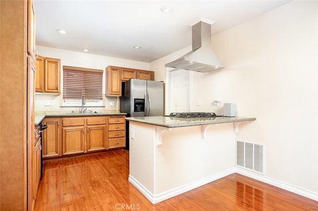 5202 Caliente Dr, Huntington Beach, CA 92649 - kitchen featuring wall chimney range hood, a peninsula, wood finished floors, a sink, and appliances with stainless steel finishes