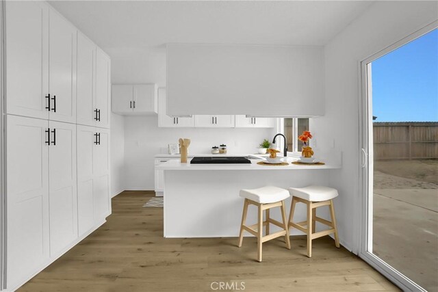 24855 Sundial Way, Moreno Valley, CA 92557 - kitchen with white cabinets, light countertops, light wood-style flooring, a peninsula, and a kitchen breakfast bar
