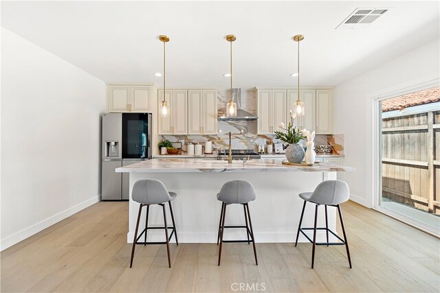 3991 Hubert Ave, Los Angeles, CA 90008 - kitchen featuring wall chimney exhaust hood, stainless steel refrigerator with ice dispenser, cream cabinetry, tasteful backsplash, and light wood-style flooring