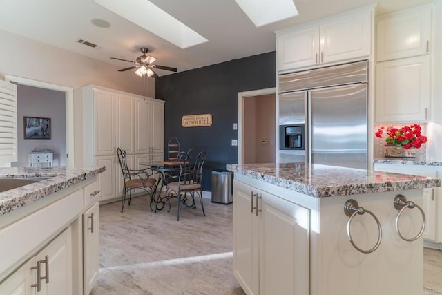 30646 Red Hawk Rd, Valley Center, CA 92082 - kitchen with stainless steel built in fridge, a skylight, light stone counters, white cabinets, and a center island