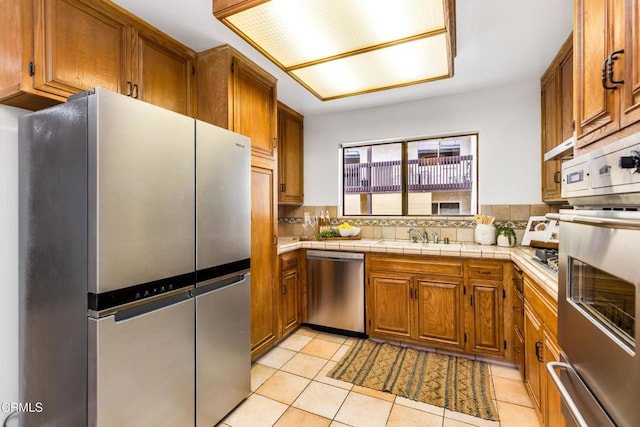 5354 Lindley Ave Unit 202, Encino, CA 91316 - kitchen with stainless steel appliances, a sink, brown cabinetry, tasteful backsplash, and light tile patterned floors