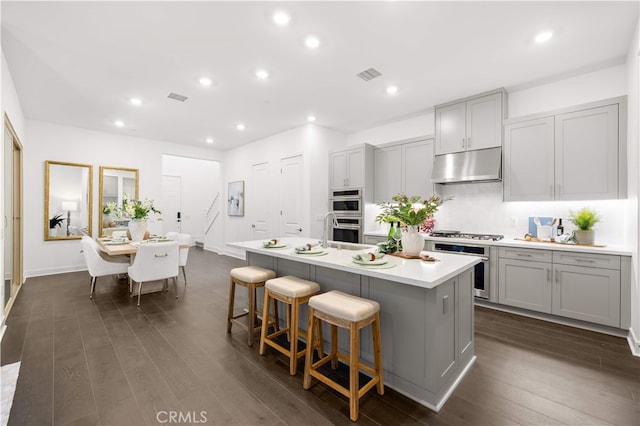 149 Great Park Blvd, Irvine, CA 92618 - kitchen featuring under cabinet range hood, gray cabinetry, a center island with sink, light countertops, and dark wood finished floors