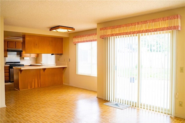 2868 Corte Caballos, Camarillo, CA 93010 - kitchen with stainless steel range with gas stovetop, brown cabinetry, under cabinet range hood, a breakfast bar, and a peninsula