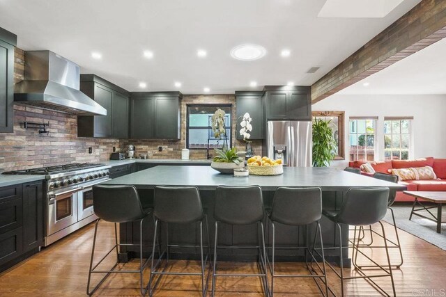 2211 Bancroft St, San Diego, CA 92104 - kitchen featuring stainless steel appliances, wall chimney exhaust hood, tasteful backsplash, a breakfast bar, and recessed lighting